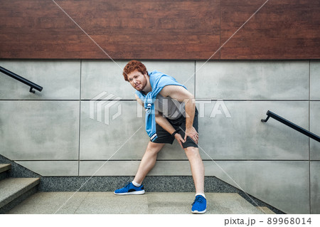 Sport injury. Injured runner, bearded freckled man with athletic body on running track feeling pain of knee. Outdoor summer activity, sport. Healthy lifestyle and workout. 89968014
