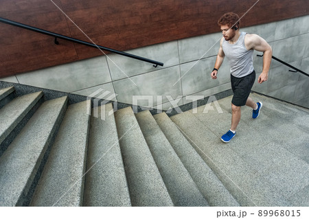 Running up on the stairs. Redhead athlete jogging on the stairs and left park. Outdoor 89968015