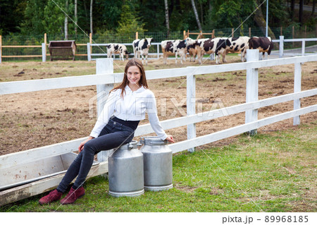 Cute young adult girl farmer, sitting on can after work. Two big can with milk. Pause after work in milk farm. Outdoor Cute young adult girl farmer, sitting on can after work. Two big can with milk. Pause after work in milk farm. Outdoor 89968185