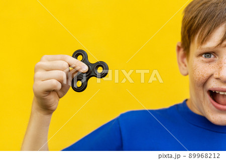 Young beautiful happy boy with freckles blue t-shirt holding fidget spinner on yellow background with amazed face... 89968212