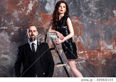 Closeup bearded businessman and ginger woman standing on old stepladder. Studio shot, isolated on vintage, old wall. 89968334