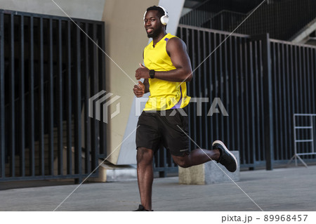 Close up portrait of toothy smiling african runner training and jogging on a summer day outdoors wearing yellow color sportswear Close up portrait of toothy smiling african runner training and jogging on a summer day outdoors wearing yellow color sportswear 89968457