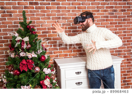 loneliness and illusion of new year. the portrait of bearded man with virtual reality glasses near new year's tree. loneliness and illusion of new year. the portrait of bearded man with virtual reality glasses near new year's tree. 89968463
