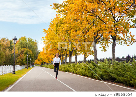 Woman running in autumn forest. Young adult girl jogging in fall colors, looking at camera and toothy smile. Woman running in autumn forest. Young adult girl jogging in fall colors, looking at camera and toothy smile. 89968654
