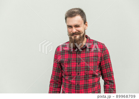Flirt and wink. Carefree bearded man winked at camera and smiling. Studio shot, gray background 89968709