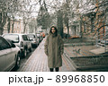 Traveling young woman in green raincoat with hood walking down street 89968850