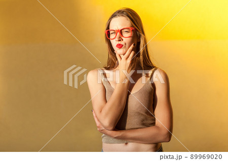 Hmm. Think about that. Young adult beautiful freckled woman, touching her chin, thinking, and looking seriously at camera. isolated on yellow background, studio shot Hmm. Think about that. Young adult beautiful freckled woman, touching her chin, thinking, and looking seriously at camera. isolated on yellow background, studio shot 89969020