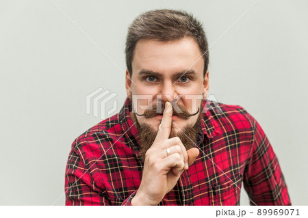 Shh sign. Anger businessman with beard and handlebar mustache looking at camera with silent sign. studio shot, on gray background. Shh sign. Anger businessman with beard and handlebar mustache looking at camera with silent sign. studio shot, on gray background. 89969071