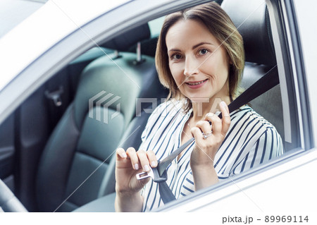 Road safety concept. Pretty business woman fastening her seat belt in a car. Outdoor photo 89969114