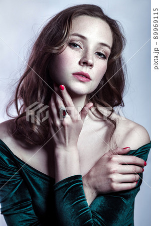 Portrait of beautiful woman with makeup, hairstyle and natural freckles on her face in green dress posing and looking at camera on gray silver background. 89969115