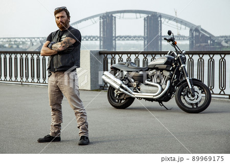 bearded motorcyclist man with his motorbike on summertime posing. 89969175