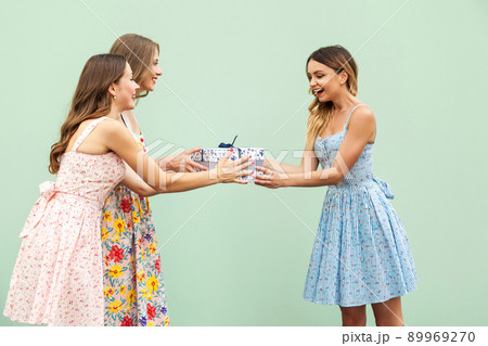 Young adult cute girl giving surprise gift to hes pretty friend. Concept of birthday and party. Isolated on green background Young adult cute girl giving surprise gift to hes pretty friend. Concept of birthday and party. Isolated on green background 89969270