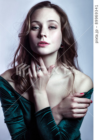 Portrait of beautiful woman with makeup, hairstyle and natural freckles on her face in green dress posing and looking at camera on gray silver background. 89969341