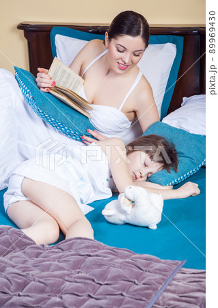 Daughter sleeping, mom read book and looking for child. Studio shot Daughter sleeping, mom read book and looking for child. Studio shot 89969430