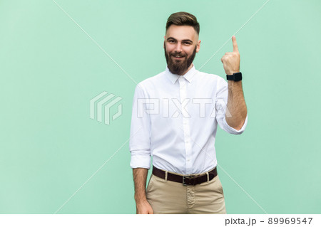Young adult businessman has an idea, pointing with finger up isolated on light green wall background. Excited guy with solution for a problem. Human face expression body language, life perception 89969547