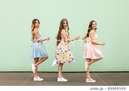 Young adult womans walking to the mall. Standing on one legs , toothy smile and looking at camera. Outdoor shot. Green wall Young adult womans walking to the mall. Standing on one legs , toothy smile and looking at camera. Outdoor shot. Green wall 89969569
