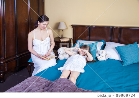 Beautiful little girl rub eyes and going to sleep. Mom looking for daughter and toothy smile. Studio shot 89969724