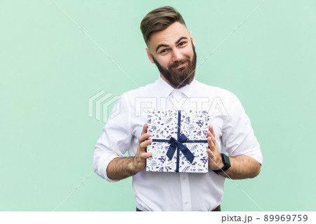 Gift with love. Interesting bearded young adult man with a gift box on light green background. Studio shot 89969759