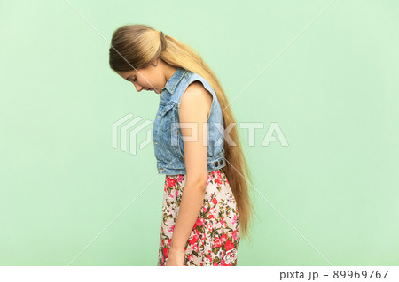 Side view of sad teenager girl, punished alone at green wall. Indoor studio shoot Side view of sad teenager girl, punished alone at green wall. Indoor studio shoot 89969767