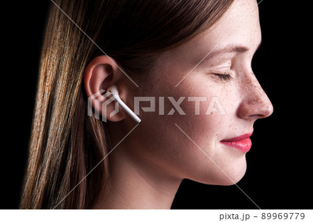Young beautiful woman with freckles and wireless earphones on her ears. studio shot on black background.. Young beautiful woman with freckles and wireless earphones on her ears. studio shot on black background.. 89969779