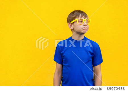 Dissatisfied and unhappy boy in yellow glasses, loking away. Isolated on yellow wall, studio shot 89970488