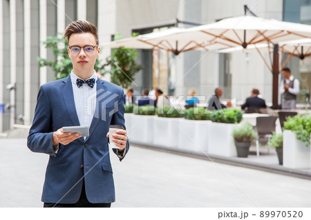 Attractive young businessman with tablet and coffee in hands on cafe background in street. looking at camera with smile. 89970520