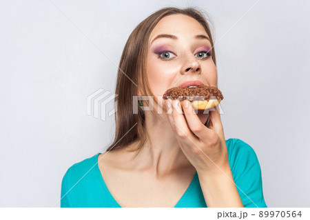 Portrait of beautiful girl with chocolate donuts. eating and looking at camera. studio shot on light gray background. Portrait of beautiful girl with chocolate donuts. eating and looking at camera. studio shot on light gray background. 89970564