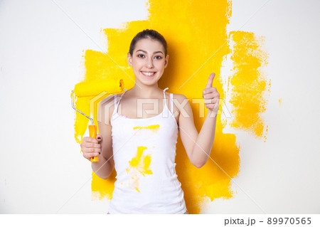 Beautiful young caucasian model in coloured shorts and white shirt and posing holding outrigger in her hands, painting the wall and looking at camera. Studio shot. Beautiful young caucasian model in coloured shorts and white shirt and posing holding outrigger in her hands, painting the wall and looking at camera. Studio shot. 89970565