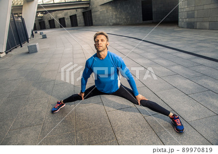 Handsome athlete man in black blue sport uniform stretching body, warming up and get ready for jogging. 89970819