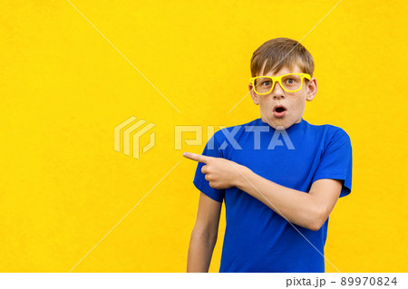 Look this! Handsome young child in shoked. Pointing away while standing isolated on light yellow background. Studio shot 89970824