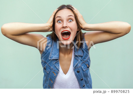 Wow! Can not be! Positive emotions and feelings. The beautiful girl shocked and wounder, touching her head her hands and looking at camera. Indoor, studio shot 89970825