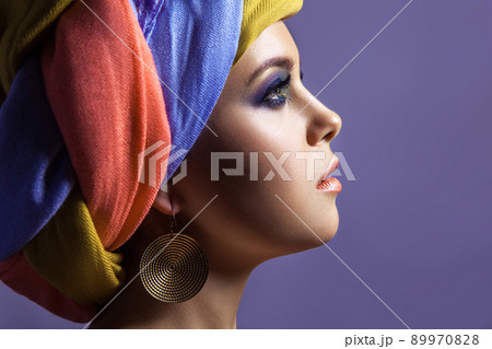 Beautiful woman with colored headwear and blue makeup, studio shot on purple background Beautiful woman with colored headwear and blue makeup, studio shot on purple background 89970828