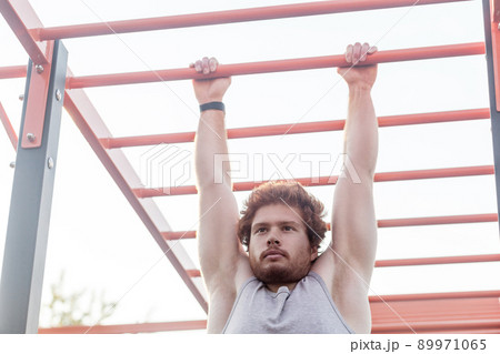 Close up. Horizontal bars. Young adult bearded redhead man, climb on bar. Outdoor 89971065