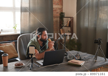 Horizontal shot of handsome Middle Eastern man sitting at table in front of laptop setting microphone to start online stream 89971161