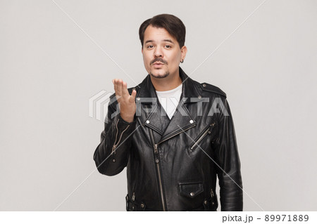 Dangerous man in leather jacket sending air kiss at camera. Studio shot, gray background Dangerous man in leather jacket sending air kiss at camera. Studio shot, gray background 89971889