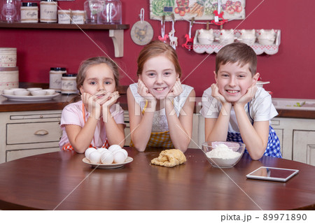 Children in the kitchen trying to learn cooking. Best friends in aprons holding pastry in their hands and making cake in kitchen and looking at each other. Studio shot. 89971890