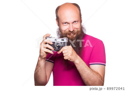 The portrait of bald bearded man photographer with pink t shirt holding classic camera. isolated on white background. studio shot. The portrait of bald bearded man photographer with pink t shirt holding classic camera. isolated on white background. studio shot. 89972041