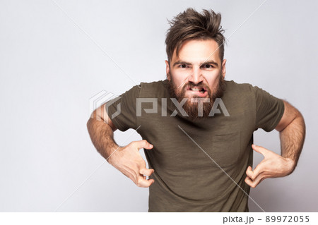 Portrait of angry crazy bearded man with dark green t shirt against light gray background. studio shot. . 89972055