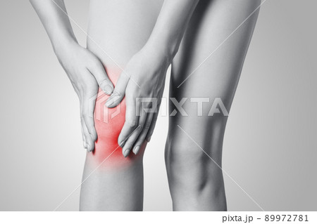 Closeup view of a young woman with knee pain on gray background. Black and white photo with red dot. 89972781