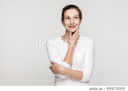 Puzzlement young adult beautiful woman embrace himself, touching chin and looking up. Studio shot, isolated on gray background Puzzlement young adult beautiful woman embrace himself, touching chin and looking up. Studio shot, isolated on gray background 89973000