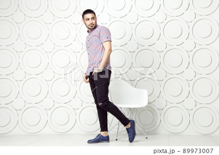 Young bearded fashion model in casual style is posing near white circle wall background. studio shot. posing and looking away with hand on packet. Young bearded fashion model in casual style is posing near white circle wall background. studio shot. posing and looking away with hand on packet. 89973007