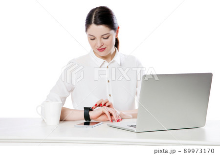 Portrait of happy attractive brunette businesswoman in white shirt sitting looking and touching her smartwatch display, reading something and smiling. indoor studio shot, isolated in white background. Portrait of happy attractive brunette businesswoman in white shirt sitting looking and touching her smartwatch display, reading something and smiling. indoor studio shot, isolated in white background. 89973170