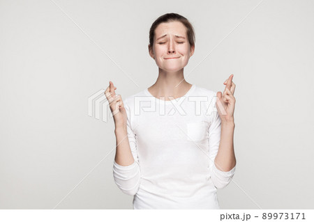 I wish some cool. Young beautiful girl closed eyes and crossed fingers. Studio shot,isolated on gray background I wish some cool. Young beautiful girl closed eyes and crossed fingers. Studio shot,isolated on gray background 89973171