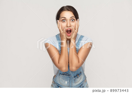 Human face expressions and emotions. Arab young adult woman holding arms on her cheeks and shocked. Isolated on gray background, studio shot Human face expressions and emotions. Arab young adult woman holding arms on her cheeks and shocked. Isolated on gray background, studio shot 89973443