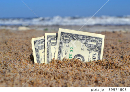 Paper bills one dollar buried in the sand on the beach against backdrop of sea close-up. American dollars cash banknotes of one dollar denomination in sand in sunny summer day. Money finance concept 89974603