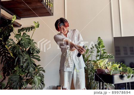 Happy guy listening to music with headphones and spraying houseplant 89978694