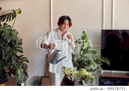 Stylish guy listening to music with headphones and watering flowerpots 89978731