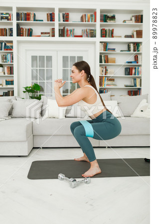 Athletic young woman doing morning exercises squatting alone in the living room, serious girl in Athletic young woman doing morning exercises squatting alone in the living room, serious girl in 89978823