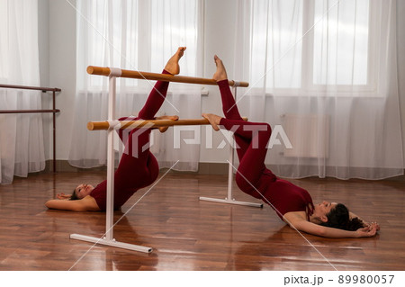 Two young womans fitness instructor in red Sportswear Leggings and Top stretching in the gym before pilates, on a yoga mat near the large window on a sunny day, female fitness yoga routine concept Two young womans fitness instructor in red Sportswear Leggings and Top stretching in the gym before pilates, on a yoga mat near the large window on a sunny day, female fitness yoga routine concept 89980057