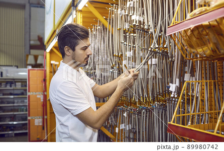 Young man shopping at a DIY store and trying to choose a new stainless steel hose Young man shopping at a DIY store and trying to choose a new stainless steel hose 89980742